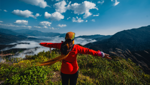 Photo: Woman in vibrant outfit embracing the stunning mountain view under a bright blue sky. | Pexels.